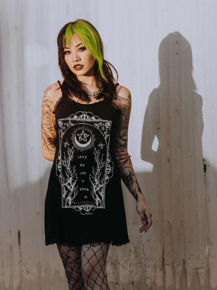A model standing outside wearing a black lace trimmed mini dress with custom Blackcraft artwork on the front.