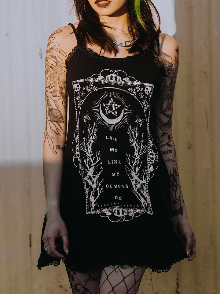 A model standing outside wearing a black lace trimmed mini dress with custom Blackcraft artwork on the front.