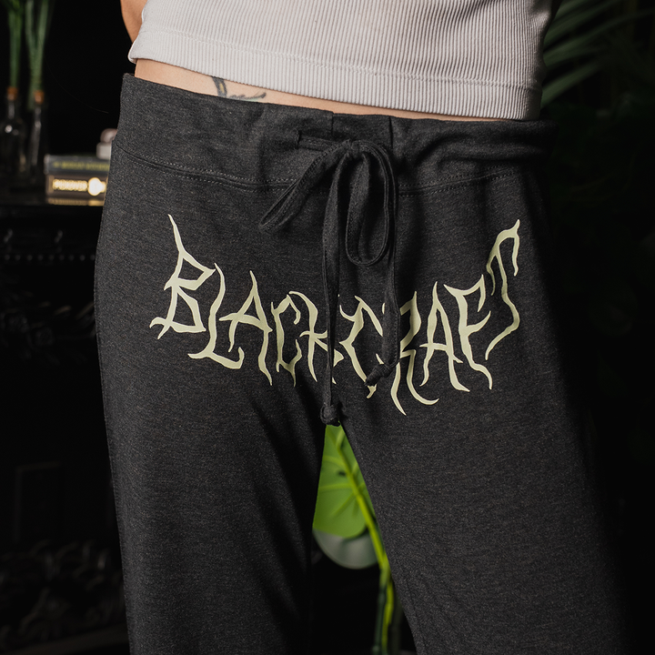 A model wearing relaxed fit, wide leg lounge pants with custom plant witch artwork at the front and along the side of the leg.