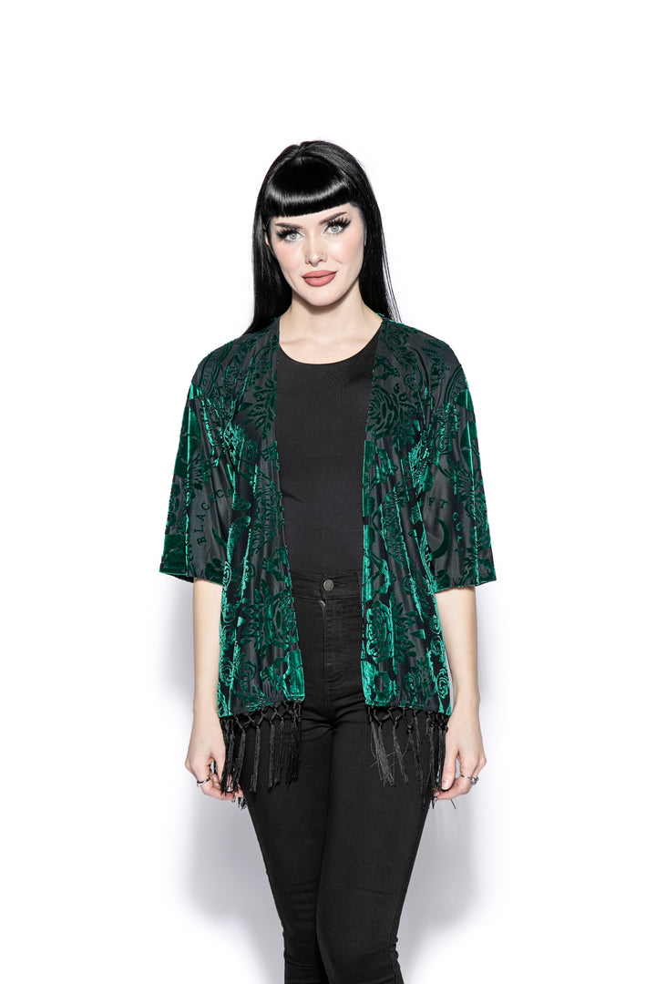 A gothic velvet kimono cover up with fringed trim, an open front, and kimono half length sleeves.