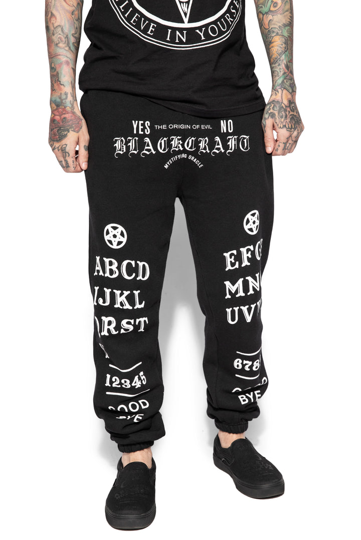 A model wearing a pair of classic fit black sweatpants with custom Blackcraft artwork along the front of each leg.