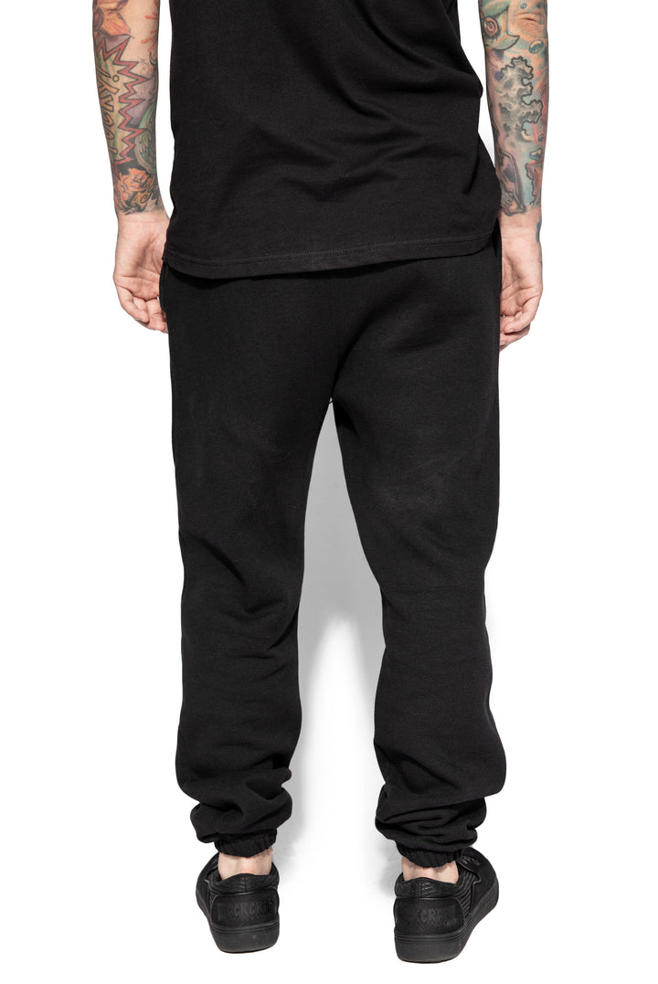 A model wearing a pair of classic fit black sweatpants with custom Blackcraft artwork along the front of each leg.