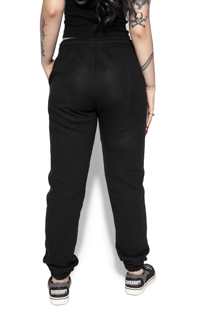 A model wearing a pair of classic fit black sweatpants with custom Blackcraft artwork along the front of each leg.