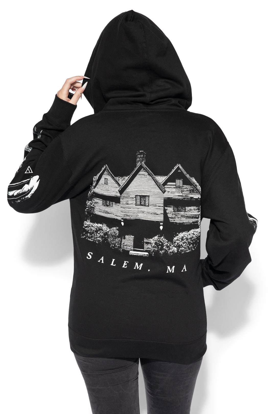 A blond model wearing a classic black zip up hoodie with Salem Massachusetts artwork along the front, back, and along the sleeves. 