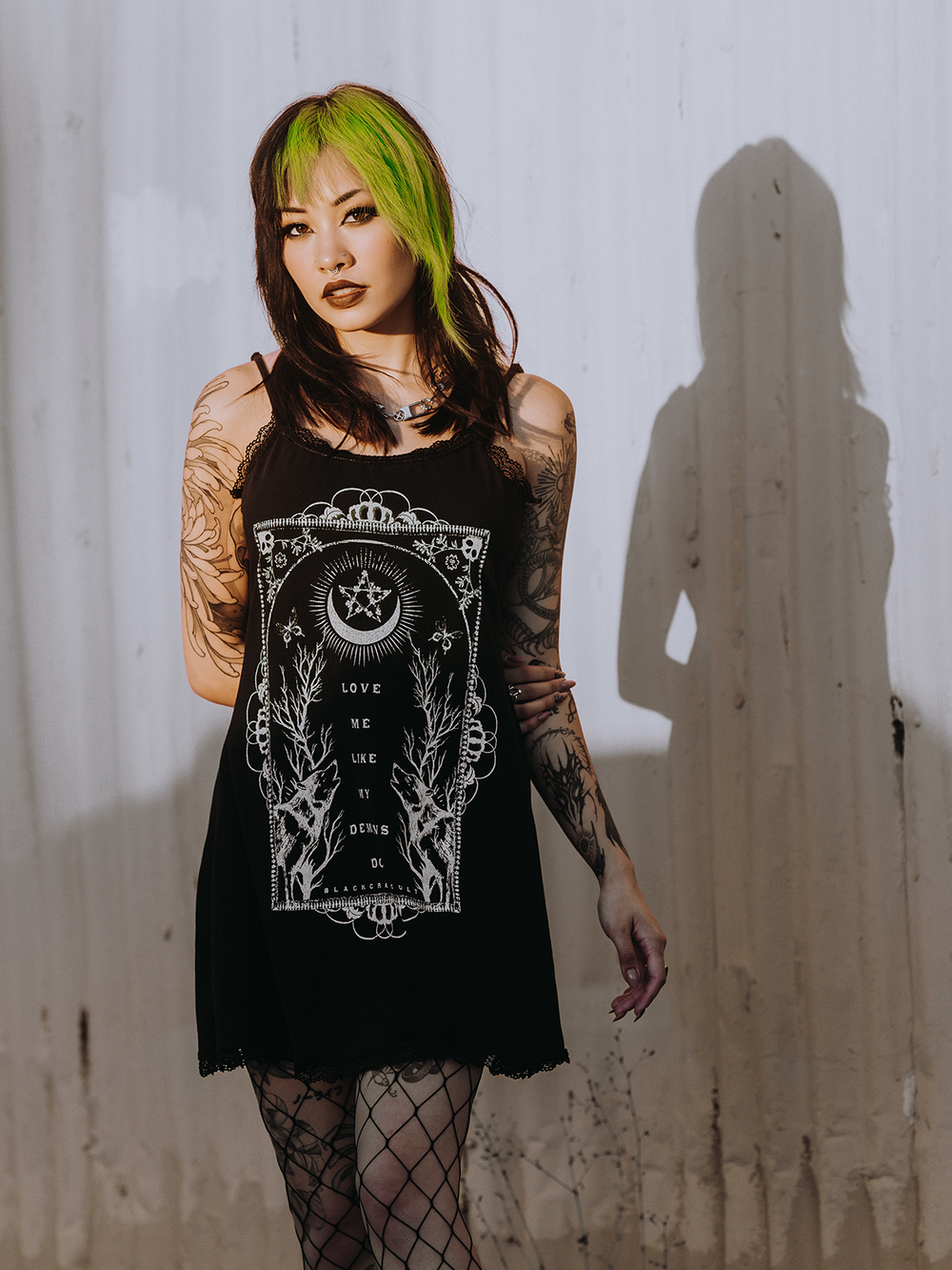 A model standing outside wearing a black lace trimmed mini dress with custom Blackcraft artwork on the front. 
