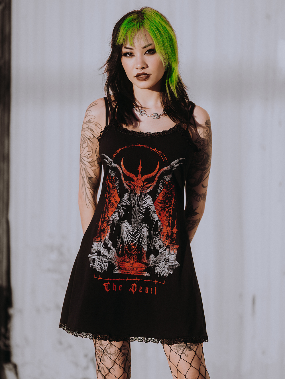 A model standing outside wearing a black lace trimmed mini dress with custom Blackcraft artwork on the front. 
