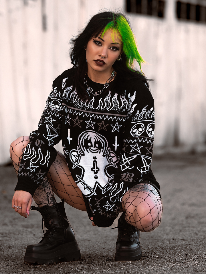 A model standing outside wearing a gothic black and white spooky gingerbread holiday sweater, from Blackcraft. 