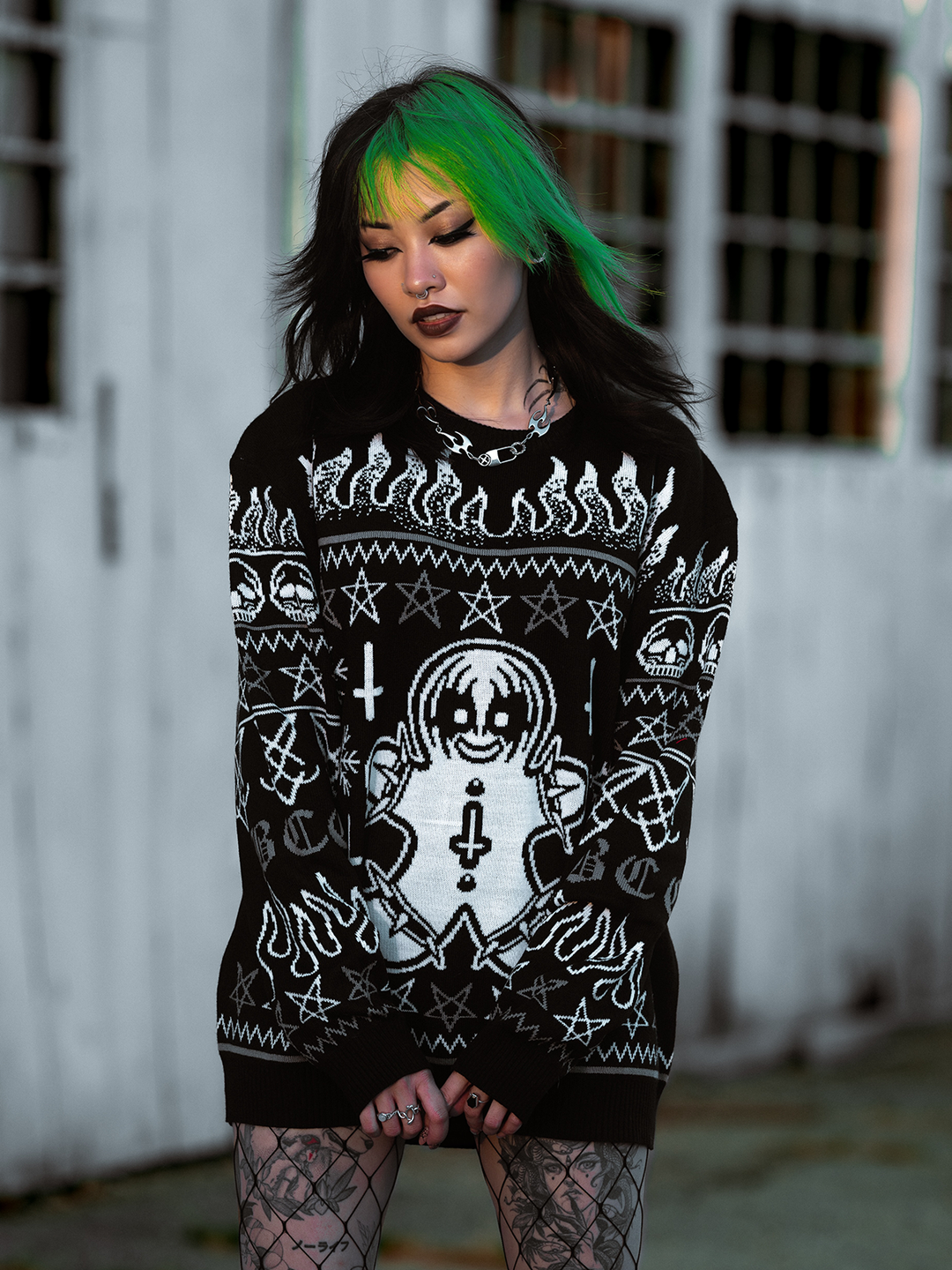 A model standing outside wearing a gothic black and white spooky gingerbread holiday sweater, from Blackcraft. 