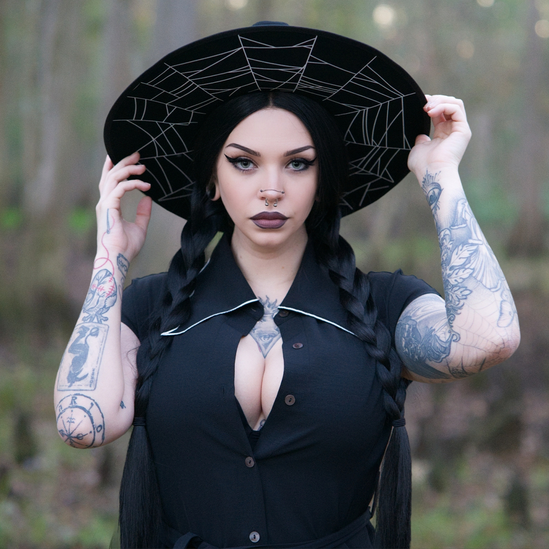 A dark haired woman standing outside wearing a black wool felted hat with cobweb design on the underside of the brim in white.