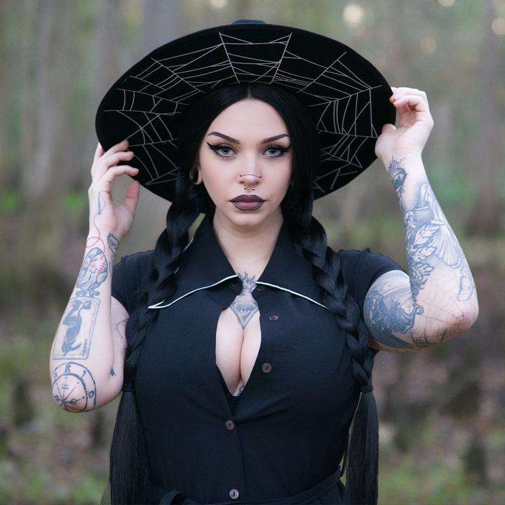 A dark haired woman standing outside wearing a black wool felted hat with cobweb design on the underside of the brim in white.