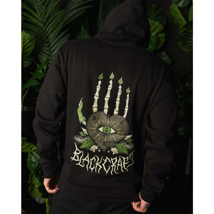 A model wearing a classic fit black Blackcraft pullover hoodie with custom plant witch artwork on the front, back, and along the sleeves.