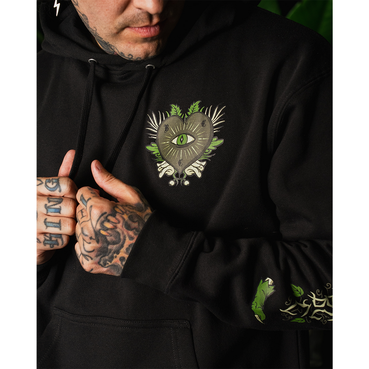 A model wearing a classic fit black Blackcraft pullover hoodie with custom plant witch artwork on the front, back, and along the sleeves.