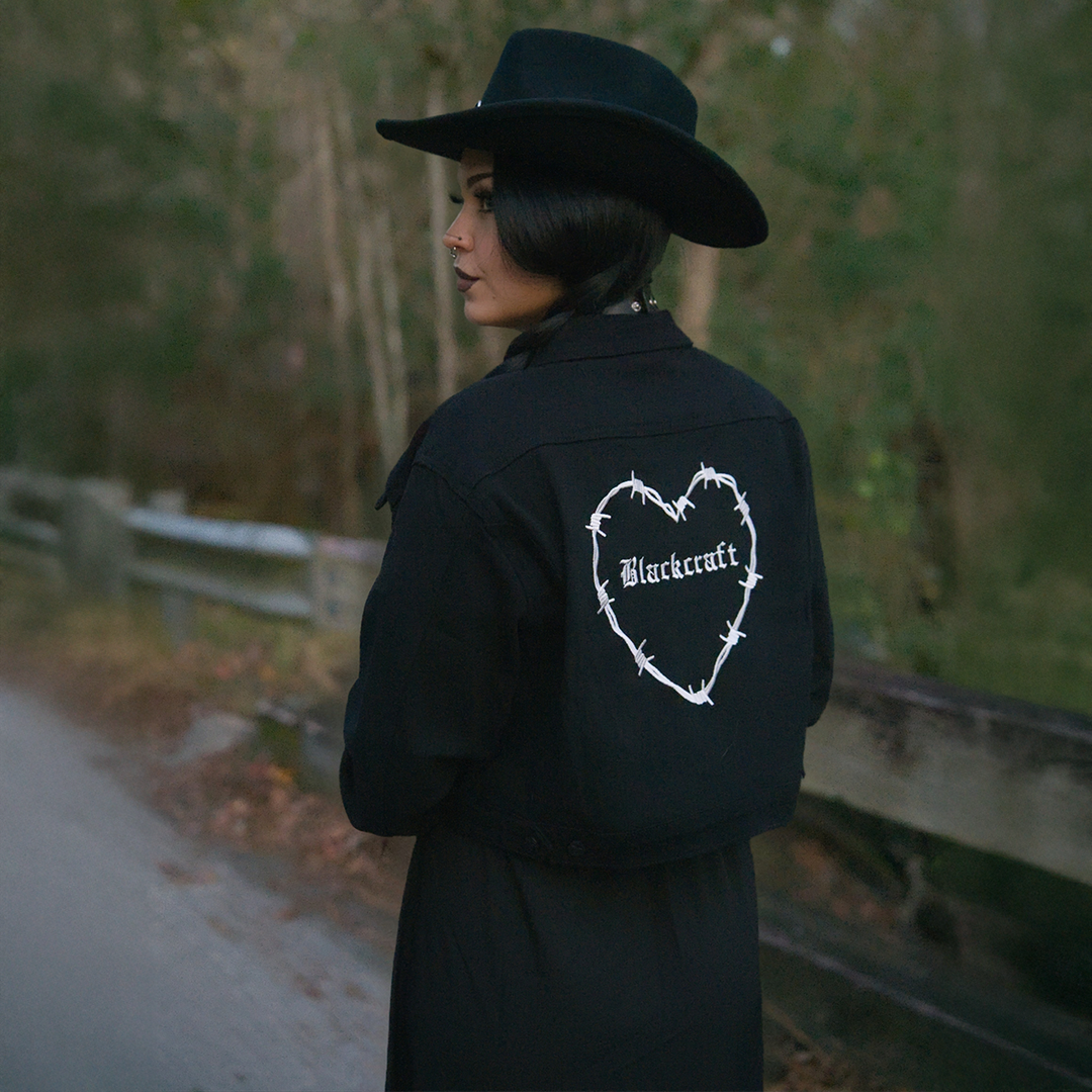 A classic black denim jacket with embroidered barbed wire heart design at the back.