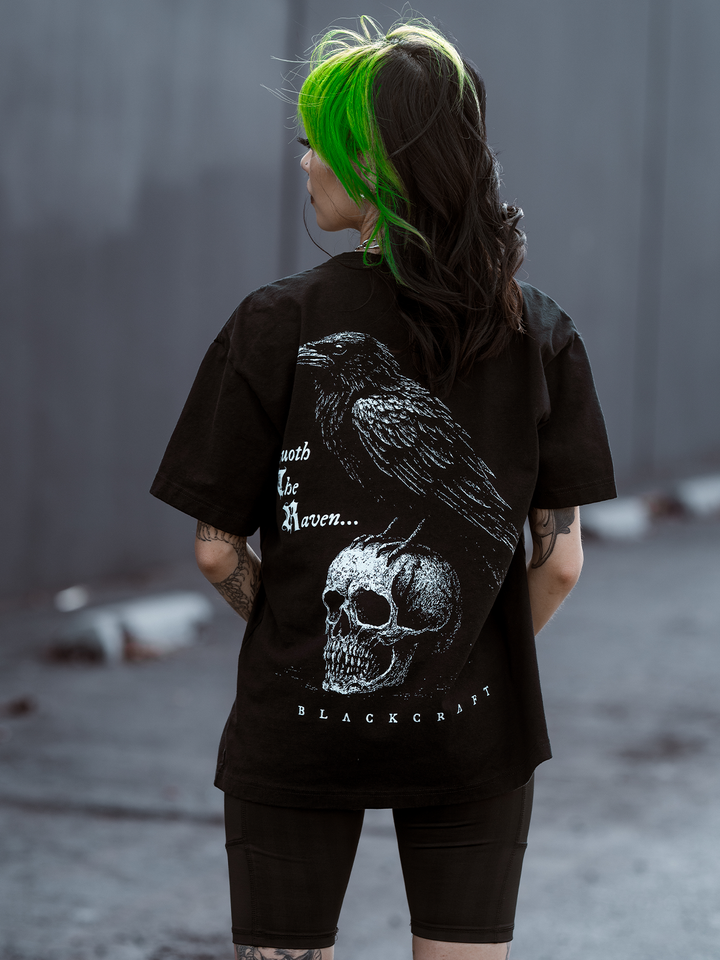 A green haired model standing outside wearing a classic black cotton boxy tee with Edgar Allen poe and the Raven artwork, from Blackcraft.