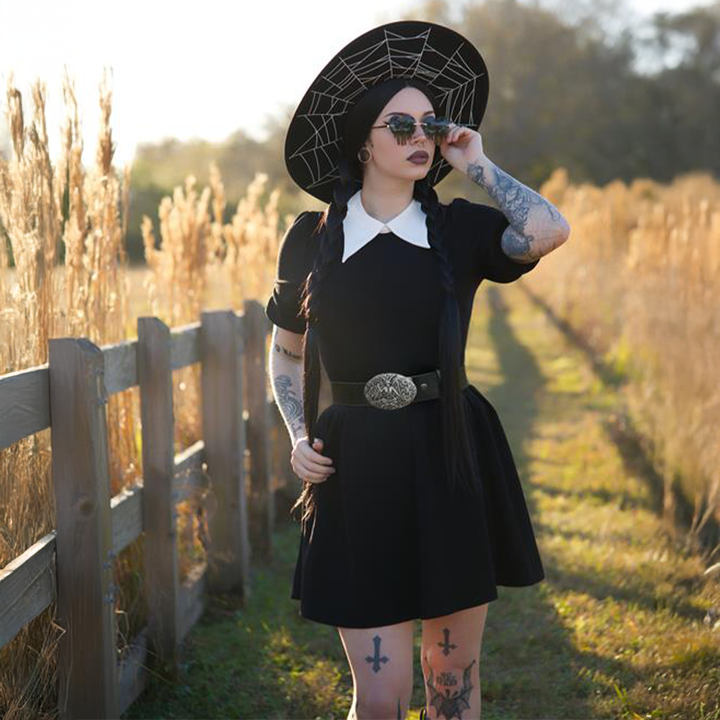 A dark haired woman standing outside wearing a black puff sleeve mini dress with contrast white pointed collar. 