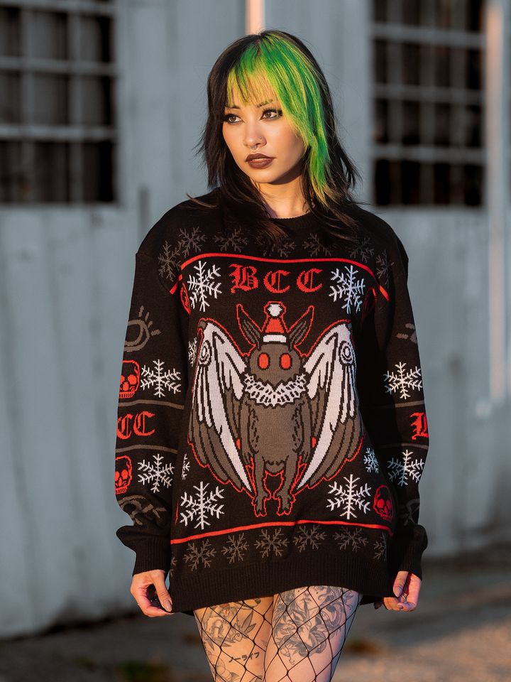 A model standing outside wearing a gothic black, red, and white spooky Mothman holiday sweater, from Blackcraft. 