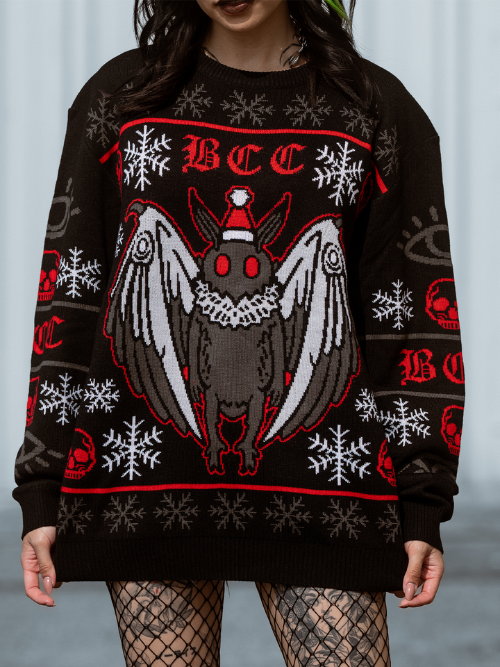 A model standing outside wearing a gothic black, red, and white spooky Mothman holiday sweater, from Blackcraft. 
