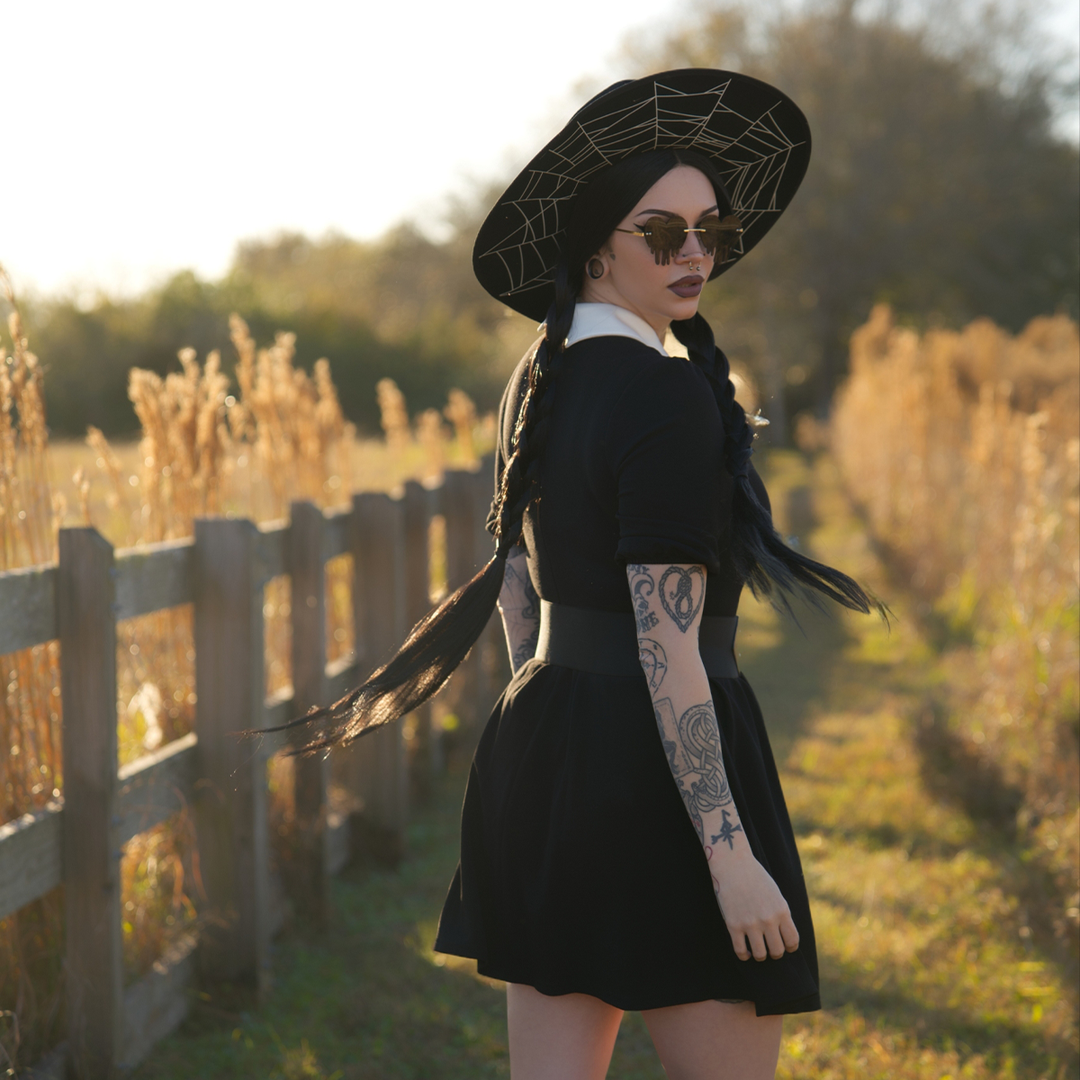 A dark haired woman standing outside wearing a black puff sleeve mini dress with contrast white pointed collar. 