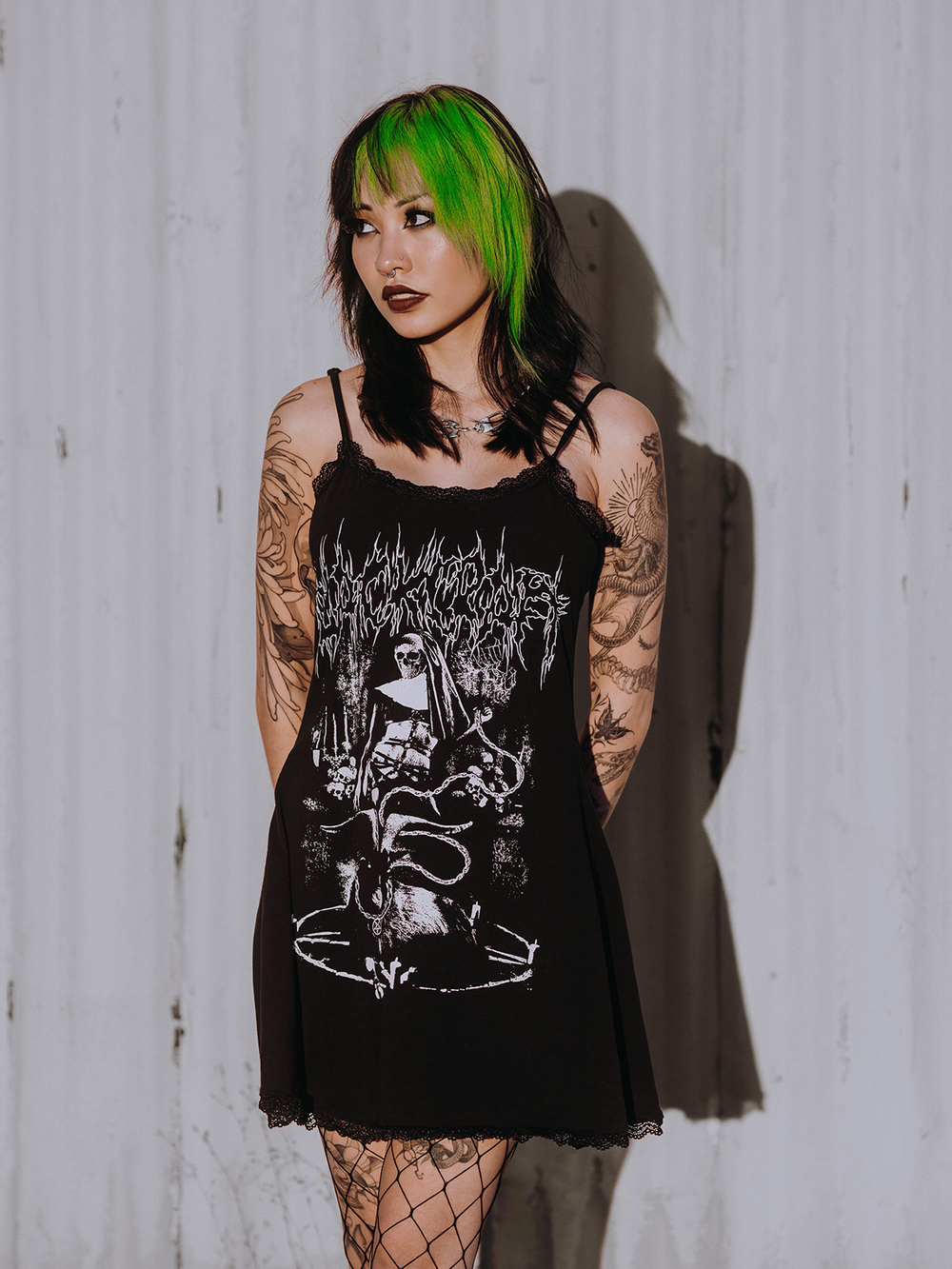 A model standing outside wearing a black lace trimmed mini dress with custom Blackcraft artwork on the front. 
