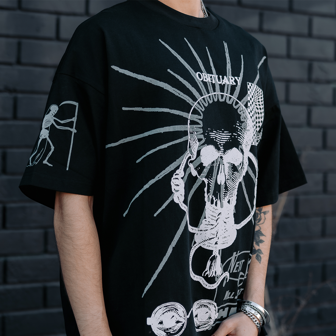 A model standing outside wearing a heavyweight oversized black tee with custom artwork on the front and right sleeve, from Blackcraft.