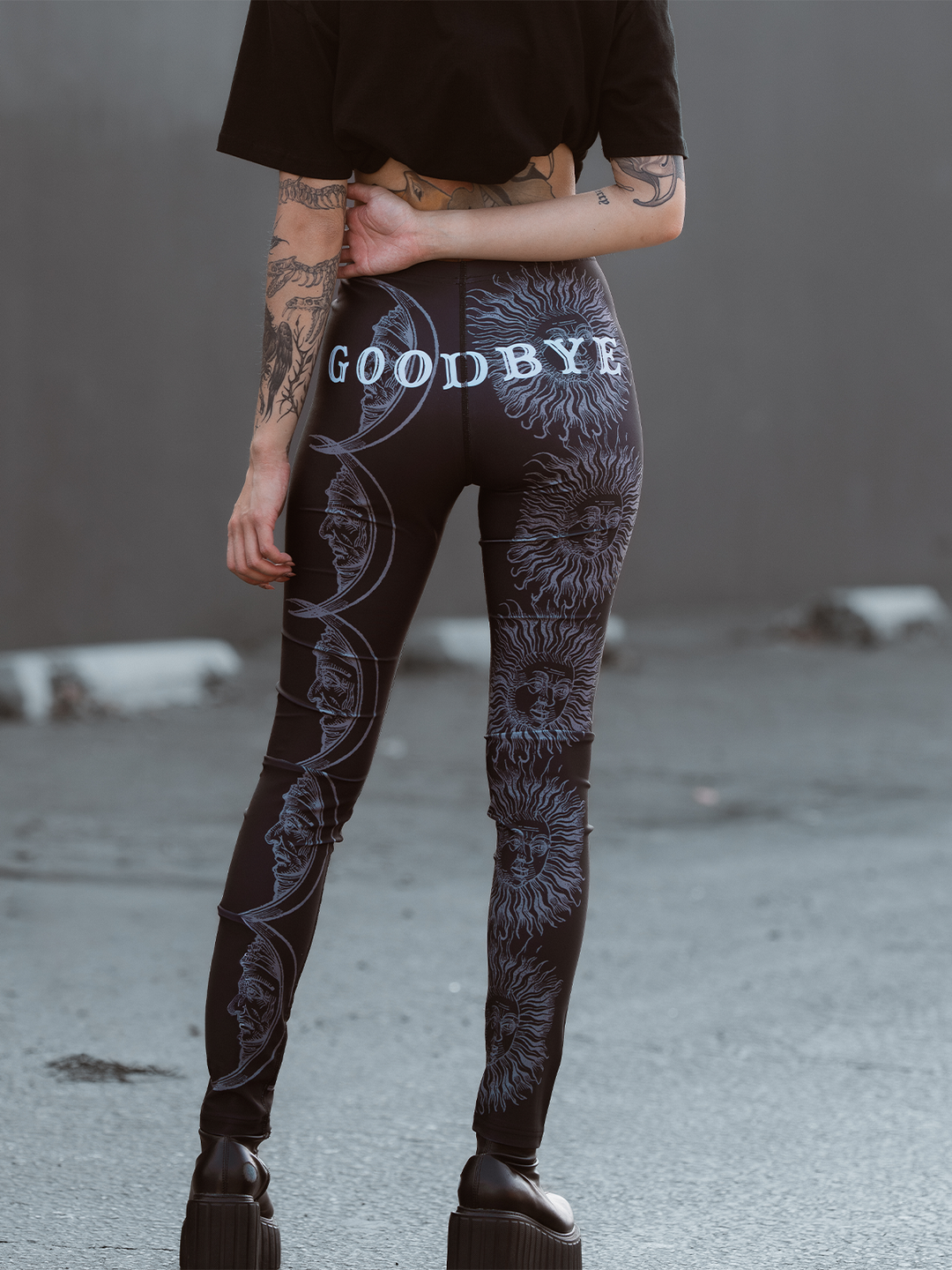 A model standing outside wearing classic women's black leggings with an allover ouija print. 