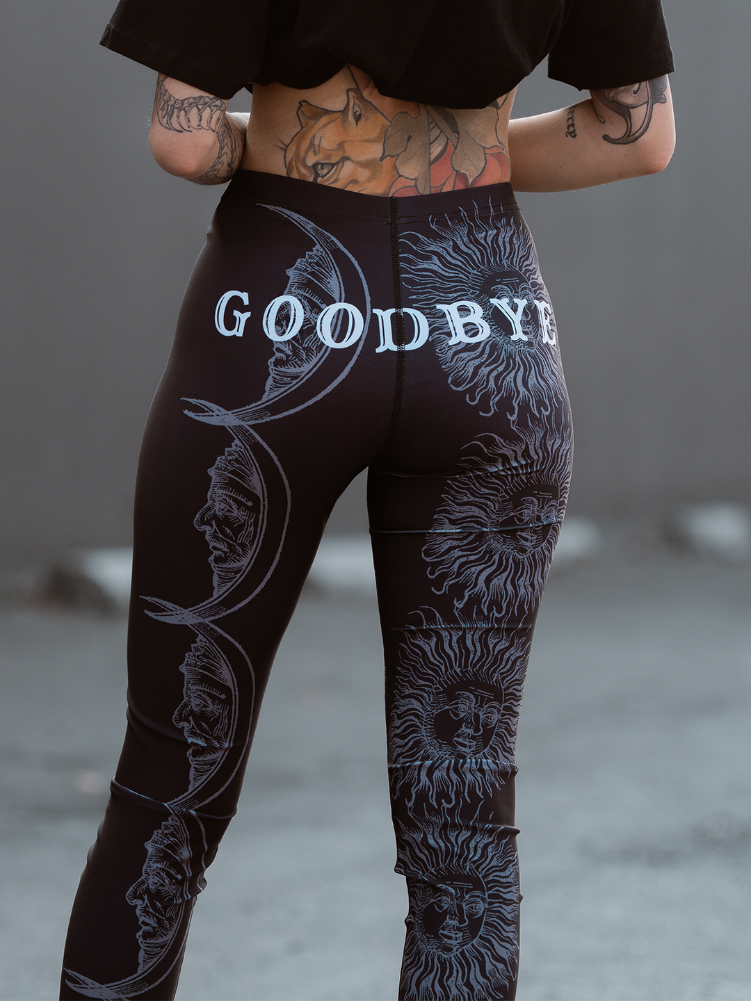 A model standing outside wearing classic women's black leggings with an allover ouija print. 