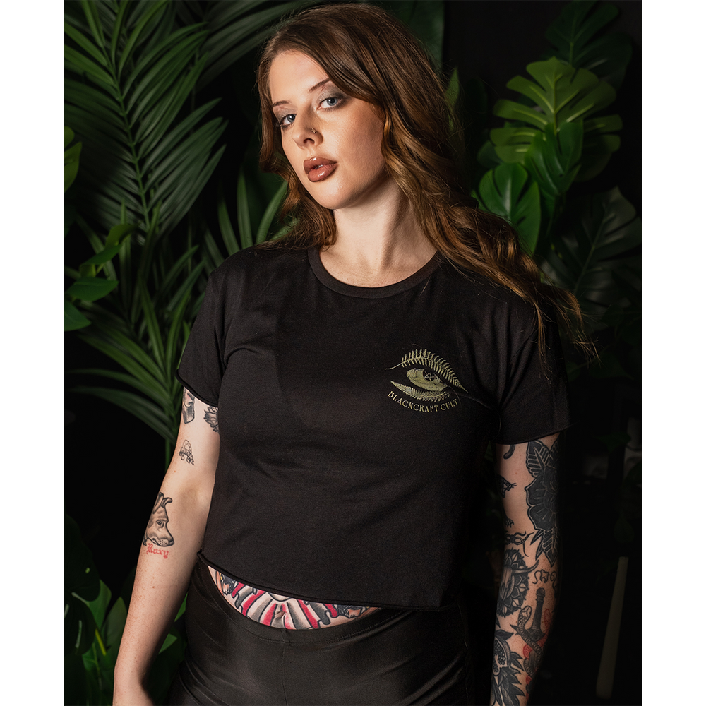A model wearing a loose fit black Blackcraft cropped top with custom plant witch artwork on the front and back.