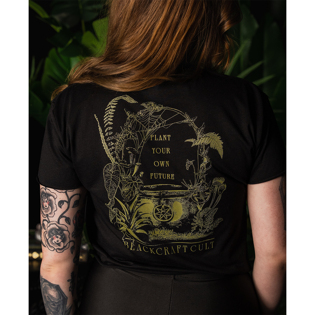 A model wearing a loose fit black Blackcraft cropped top with custom plant witch artwork on the front and back.