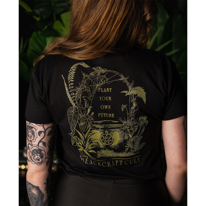 A model wearing a loose fit black Blackcraft cropped top with custom plant witch artwork on the front and back.