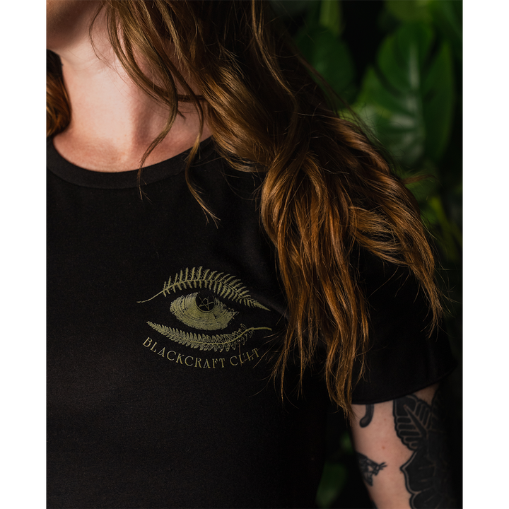 A model wearing a loose fit black Blackcraft cropped top with custom plant witch artwork on the front and back.