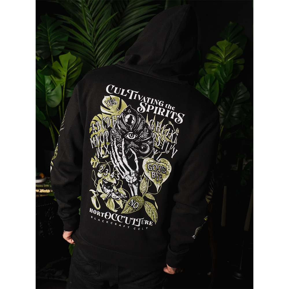 A model wearing a classic fit black Blackcraft zip up hoodie with custom plant witch artwork on the front, back, and along the sleeves.