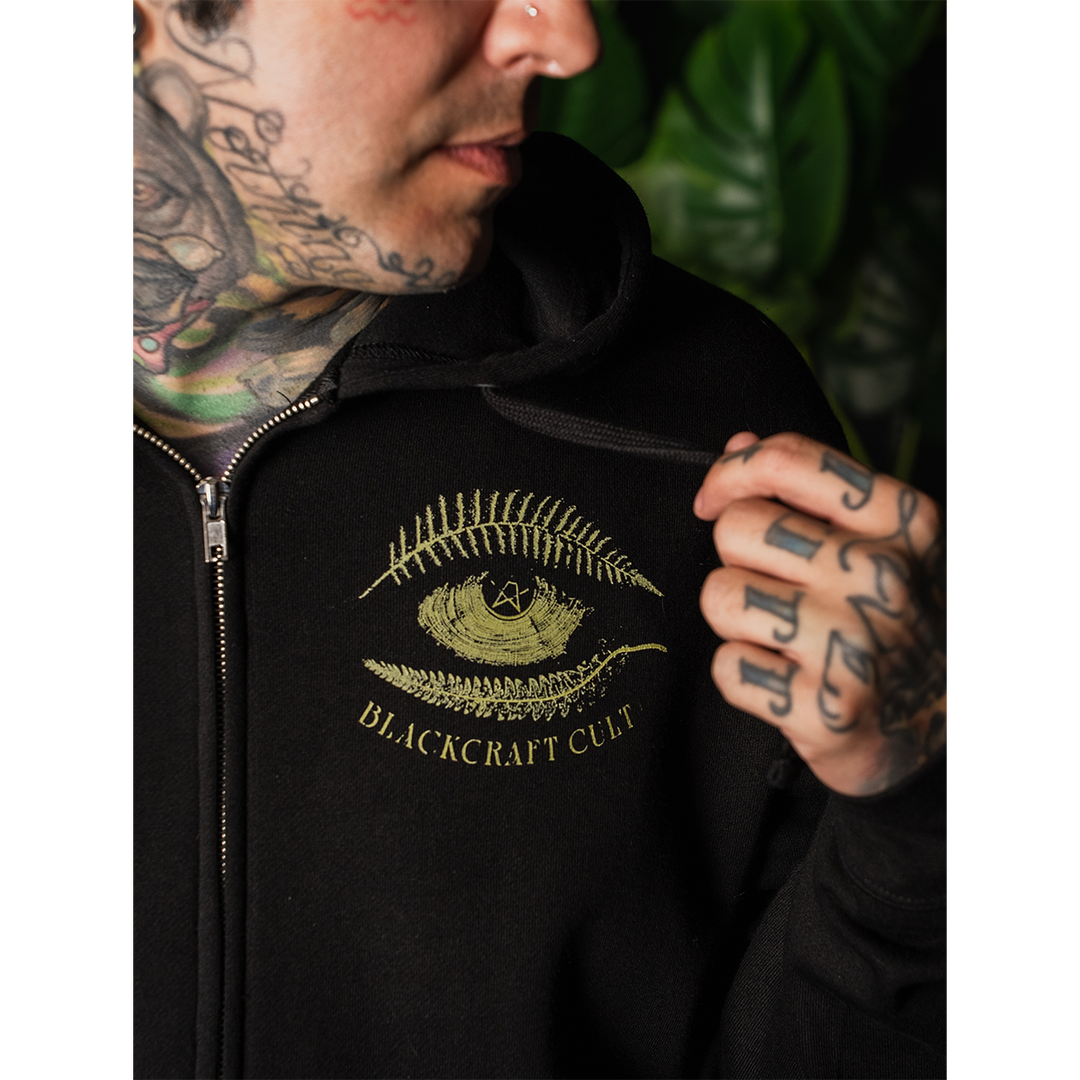 A model wearing a classic fit black Blackcraft zip up hoodie with custom plant witch artwork on the front, back, and along the sleeves.