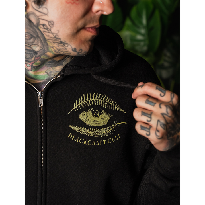 A model wearing a classic fit black Blackcraft zip up hoodie with custom plant witch artwork on the front, back, and along the sleeves.