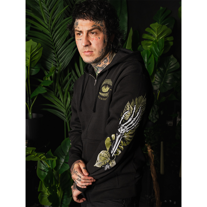 A model wearing a classic fit black Blackcraft zip up hoodie with custom plant witch artwork on the front, back, and along the sleeves.