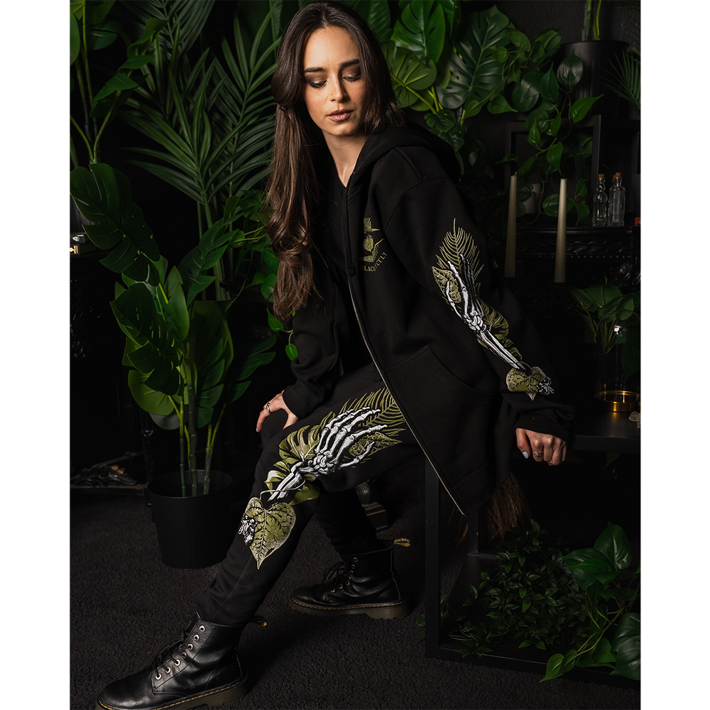 A model wearing classic black joggers with custom plant witch artwork along the sides, from Blackcraft.