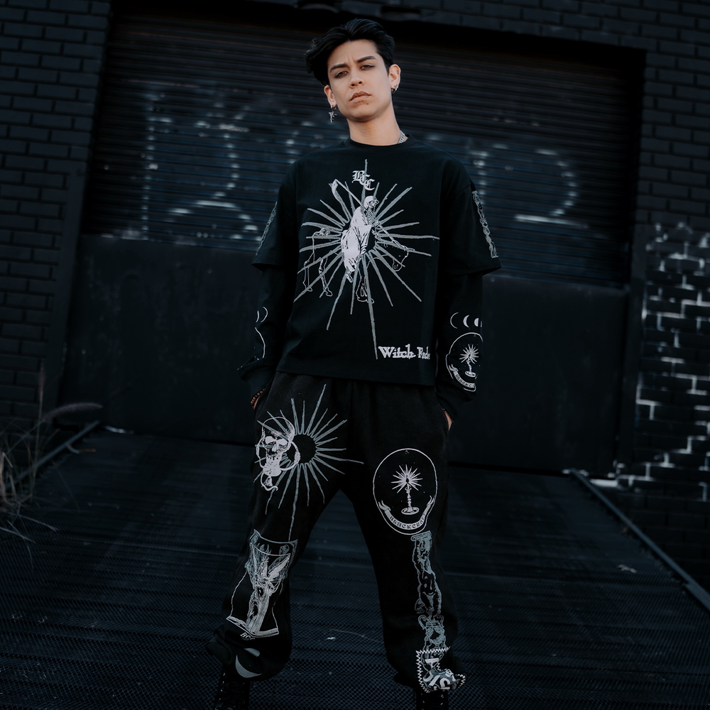 A model standing outside wearing classic sweatpants in a washed black with custom Blackcraft artwork on the front of both legs. 