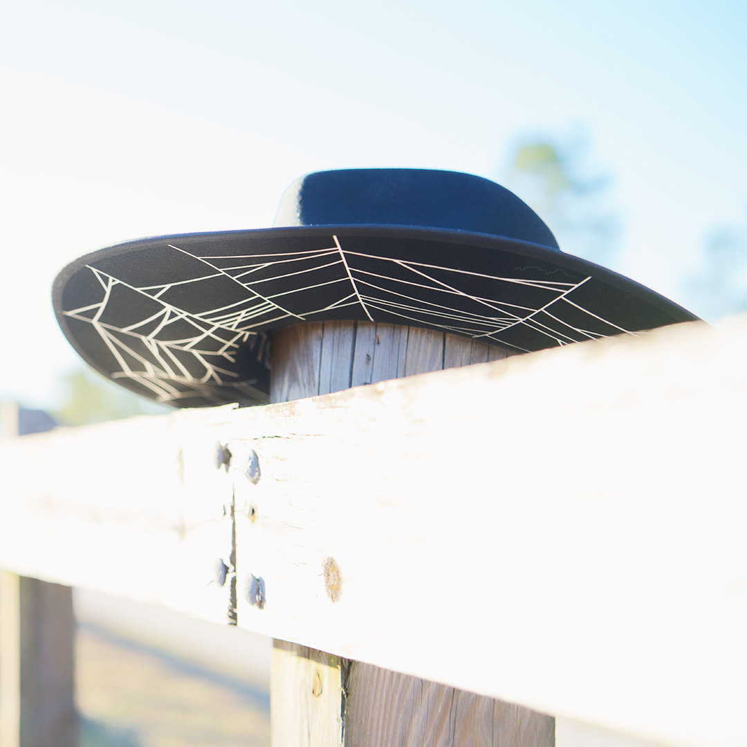 A gothic black wool felted hat with white cobweb detail at the inner brim.