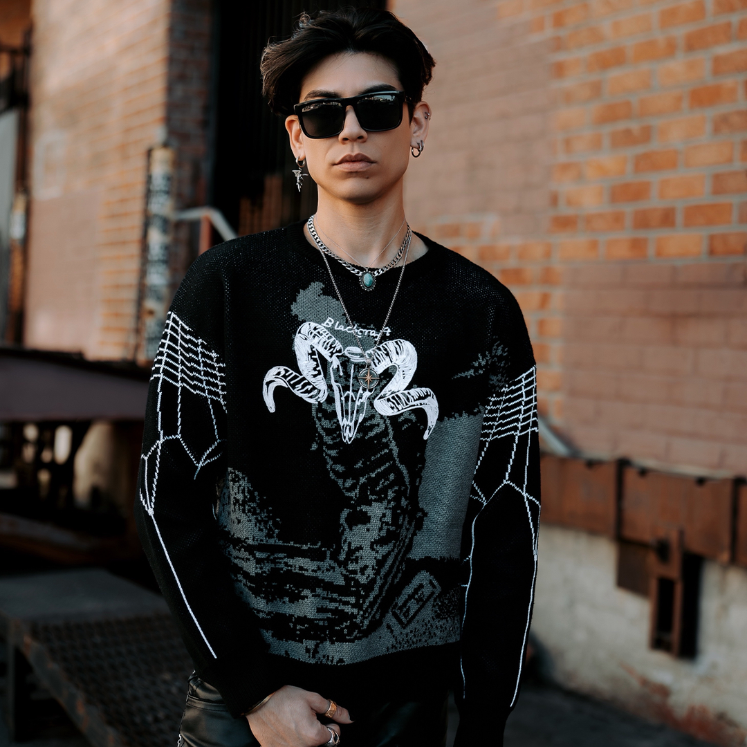 A model standing outside wearing a black pullover sweater with a knit jacquard grey and white goat skeleton design.