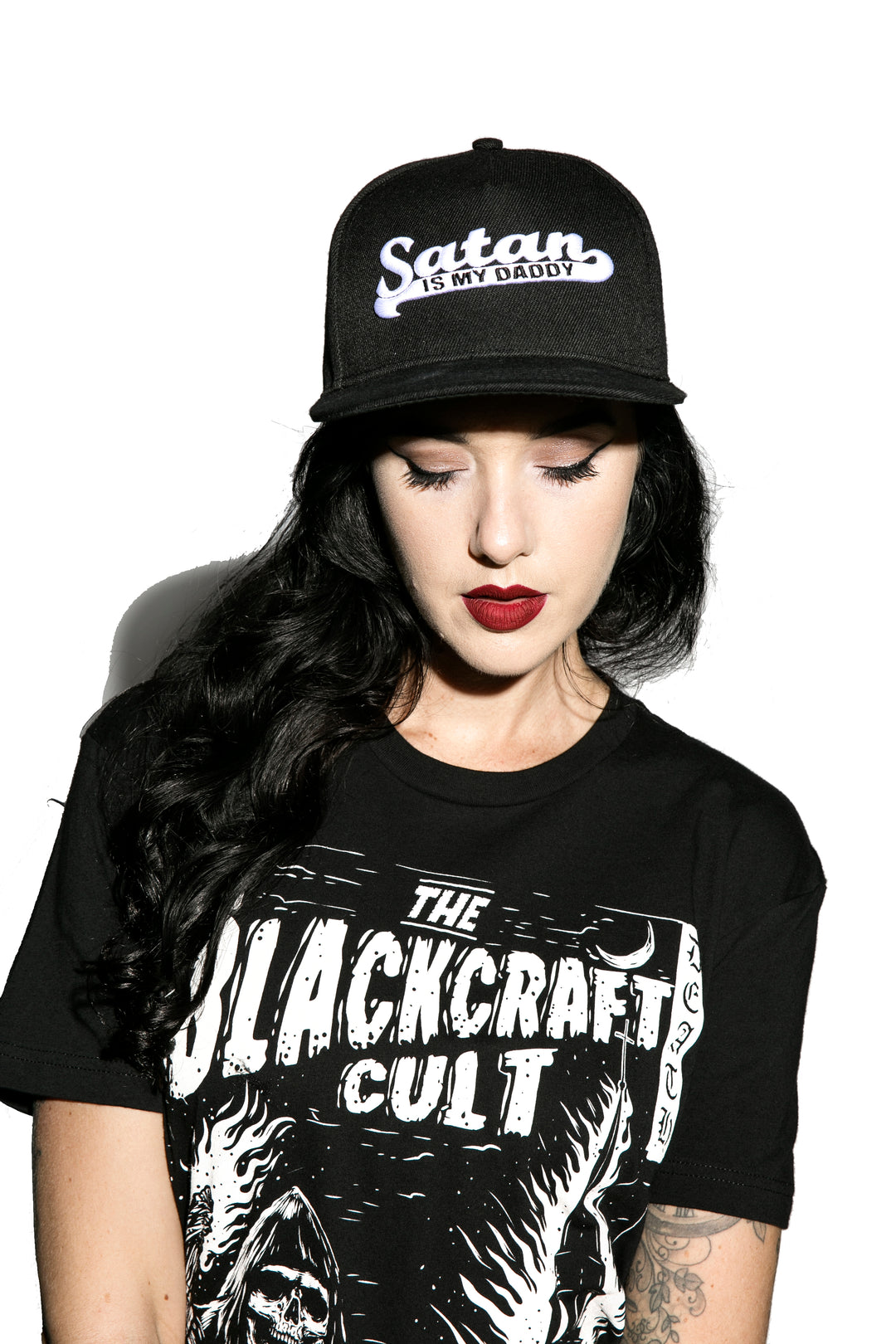 A model wearing a black snapback hat with white embroidered Satan is my Daddy on the front. 