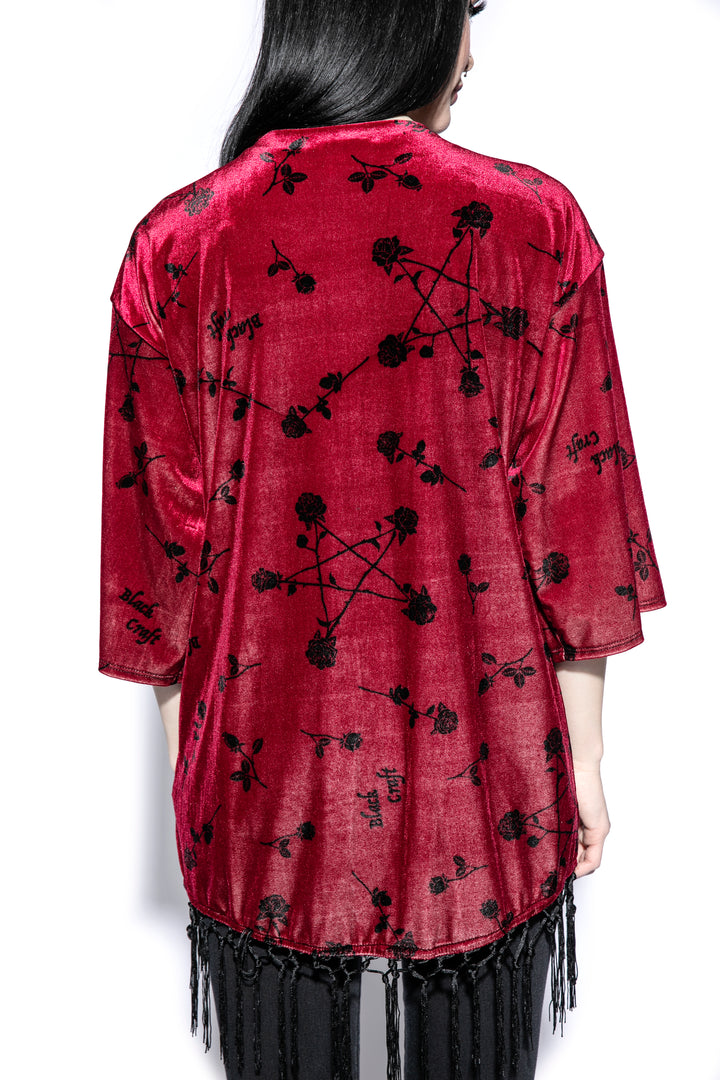 A gothic velvet kimono cover up with fringed trim, an open front, and kimono half length sleeves.
