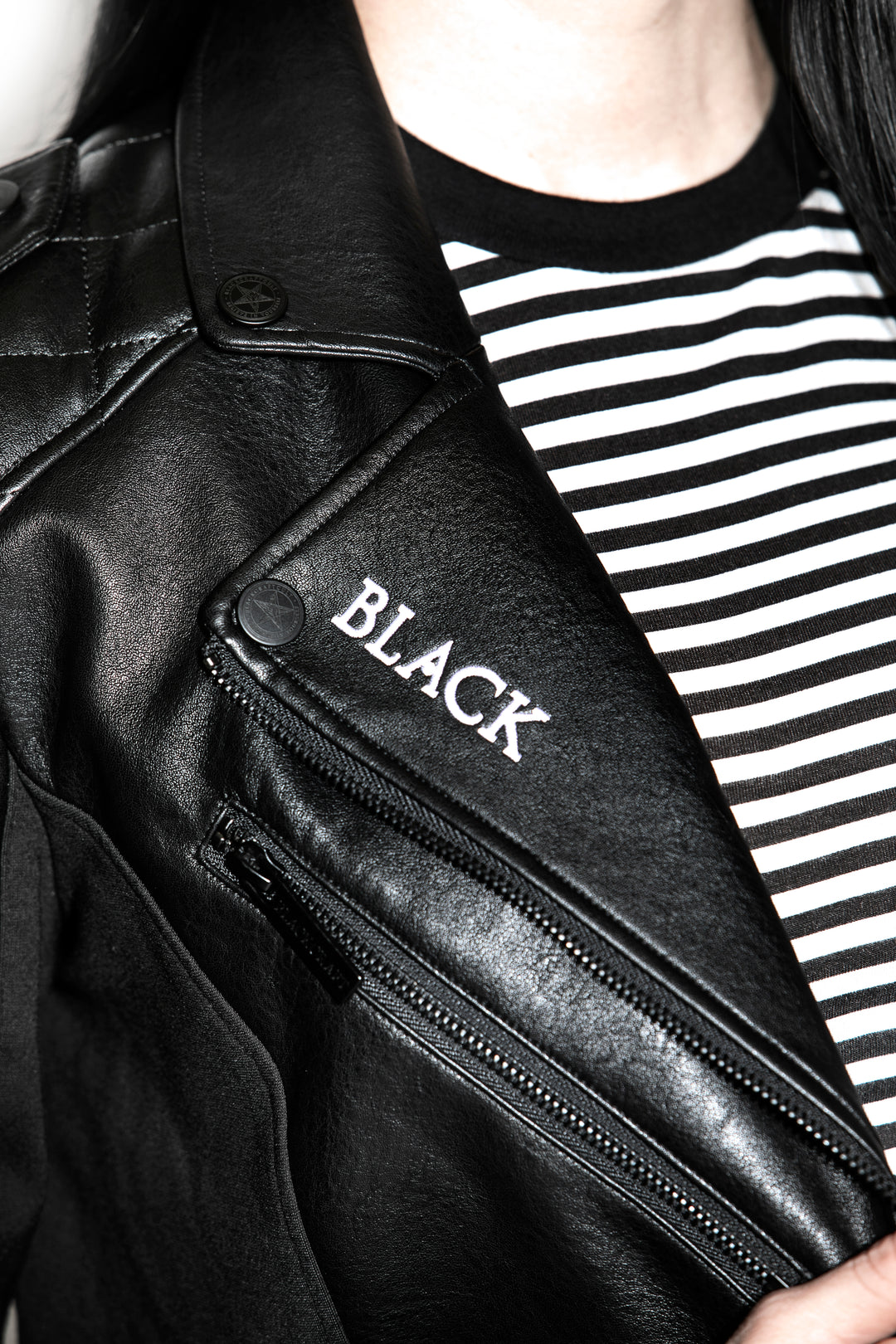 A black haired model wearing a classic black faux leather jacket from Blackcraft.
