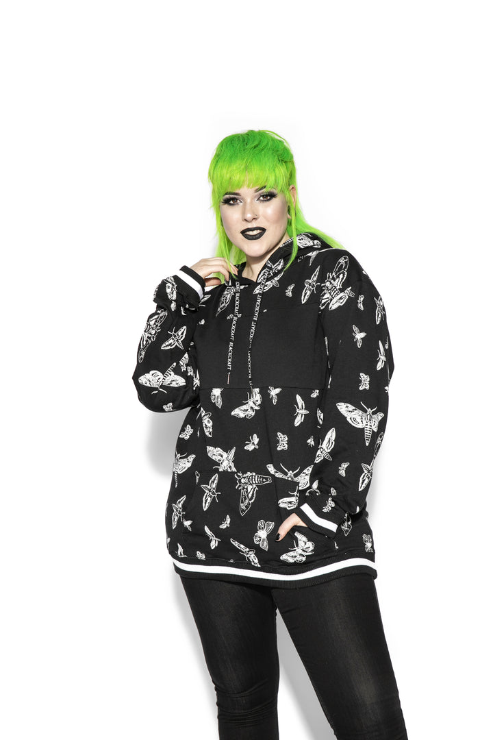 A model wearing a black and white pullover hoodie with custom Blackcraft moth artwork