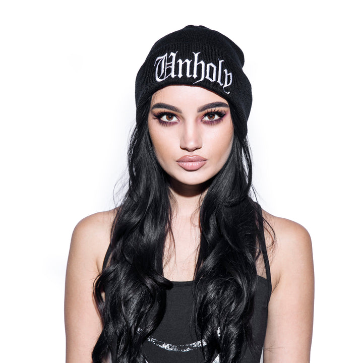 Model wearing a black beanie with unholy embroidery on front flap.
