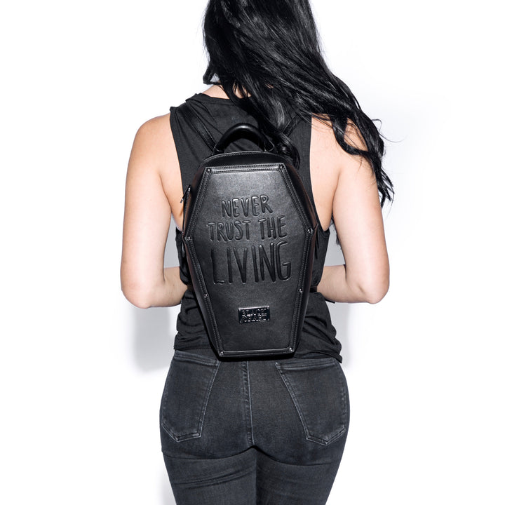 Black faux leather coffin shaped backpack with Never Trust the Living embossed on front. 