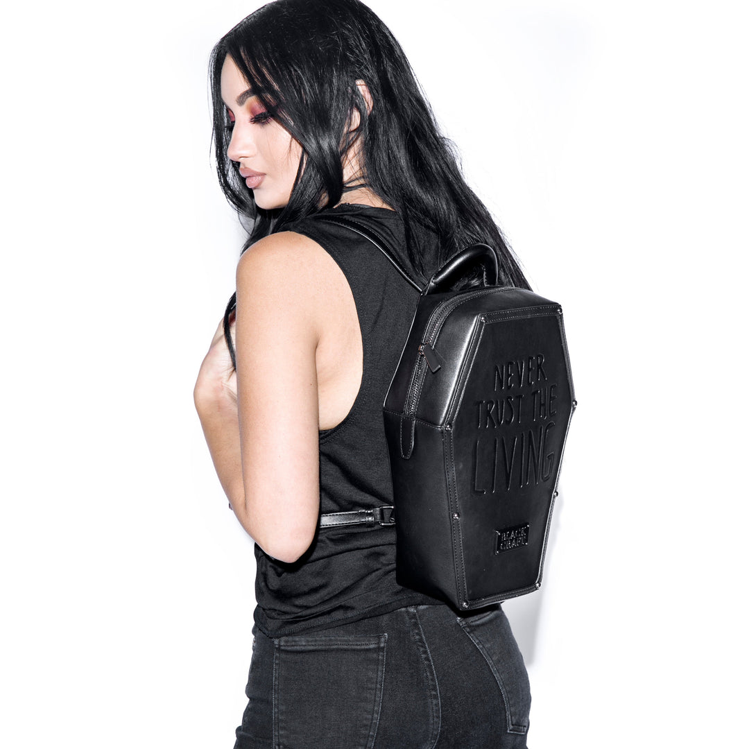 Black faux leather coffin shaped backpack with Never Trust the Living embossed on front. 