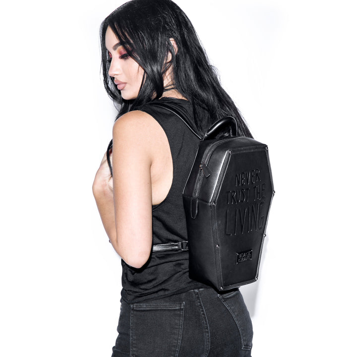 Black faux leather coffin shaped backpack with Never Trust the Living embossed on front. 