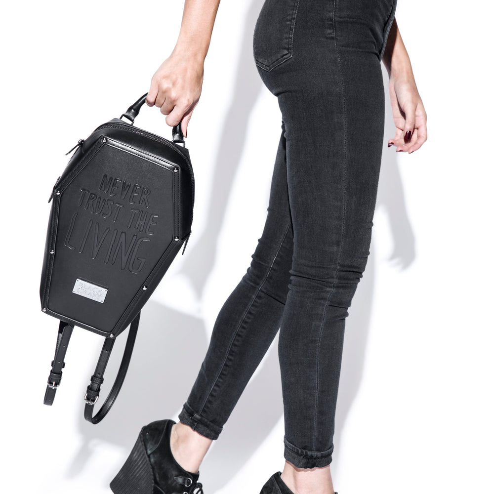 Black faux leather coffin shaped backpack with Never Trust the Living embossed on front. 
