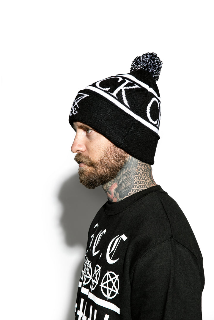 Model wearing a black bobble beanie with Blackcraft across the circumference.