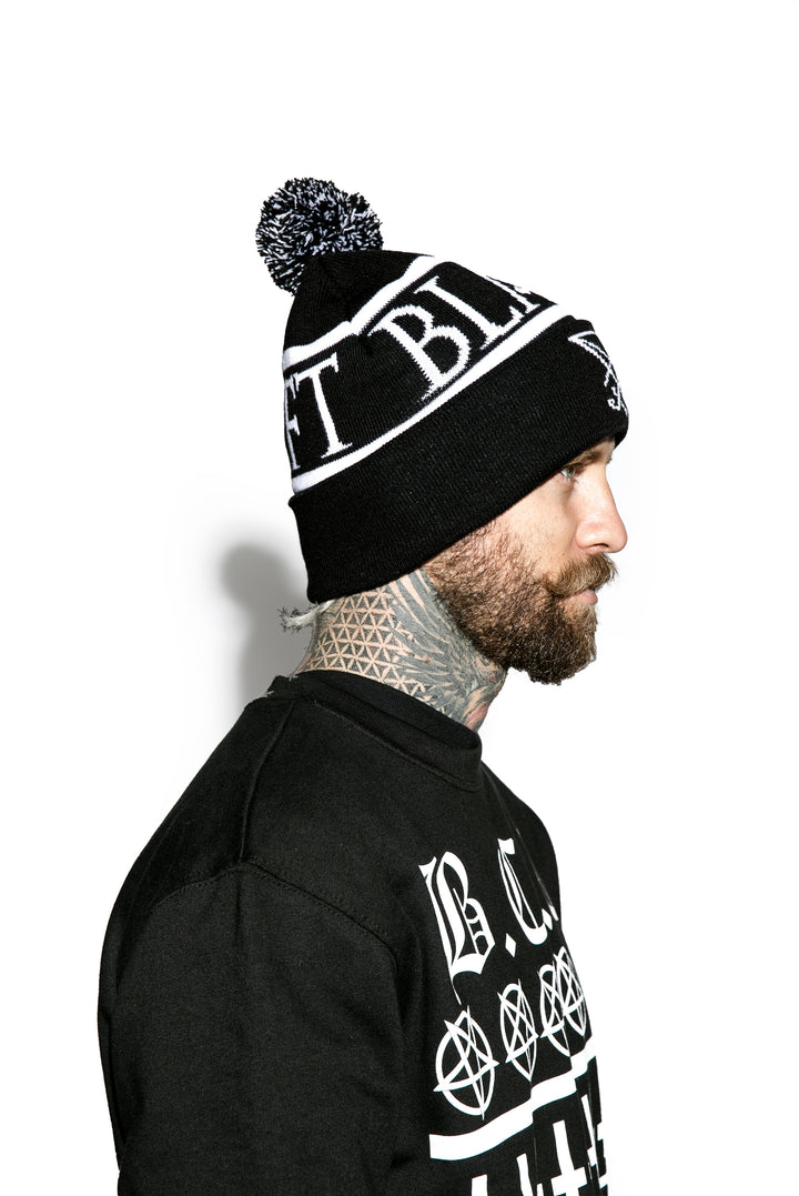 Model wearing a black bobble beanie with Blackcraft across the circumference.
