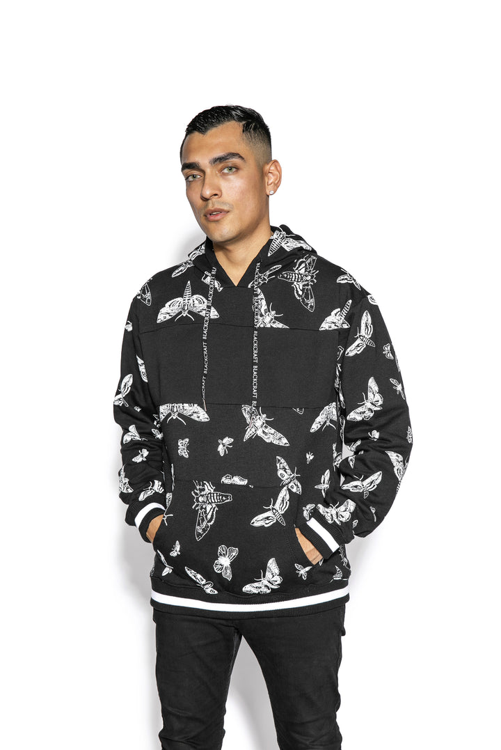 A model wearing a black and white pullover hoodie with custom Blackcraft moth artwork